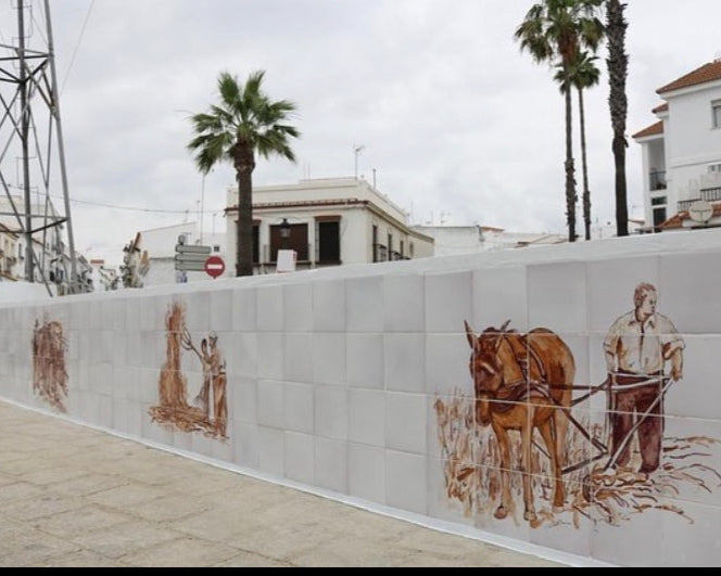 Abrevadero público en Cartaya (Huelva) con dos paños cerámicos y escenas de labranza en tonos sepia — vidriado sobre opaco.